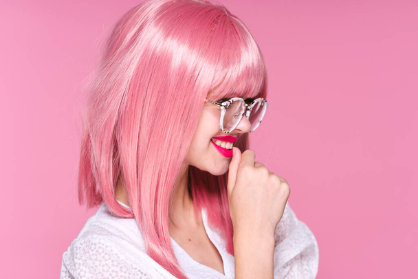 Νεαρή όμορφη γυναίκα με ροζ περούκα και γυαλιά σε ροζ φόντο - Φωτογραφία, εικόνα