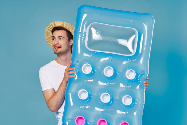 Studio shot of young man tourist with inflatable mattress on blue background - Zdjęcie, obraz