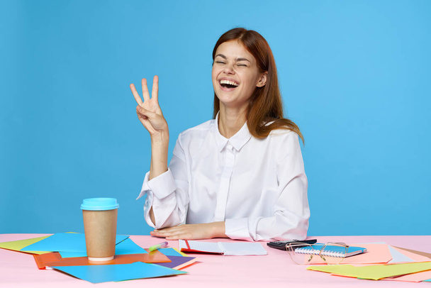 młoda piękna bizneswoman siedzi przy biurku w biurze pokazując trzy palce  - Zdjęcie, obraz