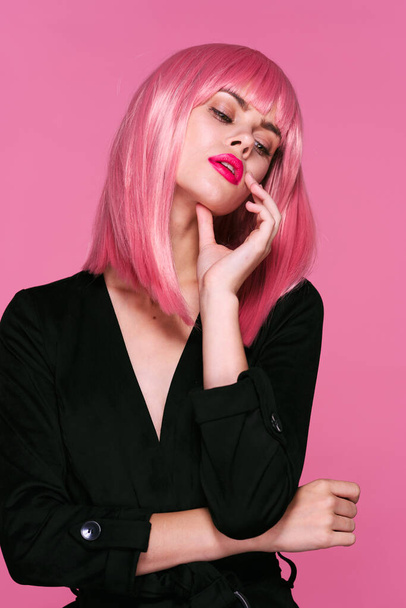 Νεαρή όμορφη γυναίκα με ροζ περούκα που κοιτάζει κάτω σε ροζ φόντο - Φωτογραφία, εικόνα