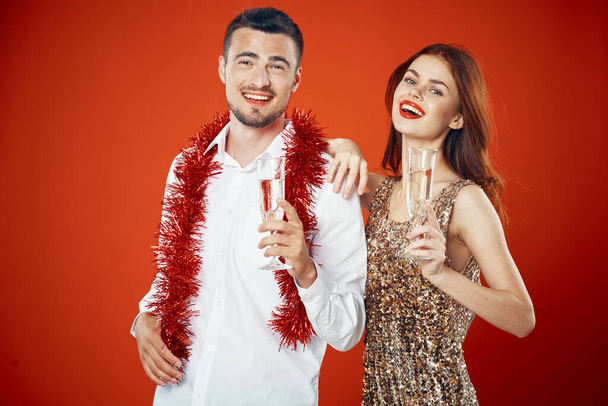 Young beautiful couple holding champagne  on red background, looking at camera  - Fotografie, Obrázek