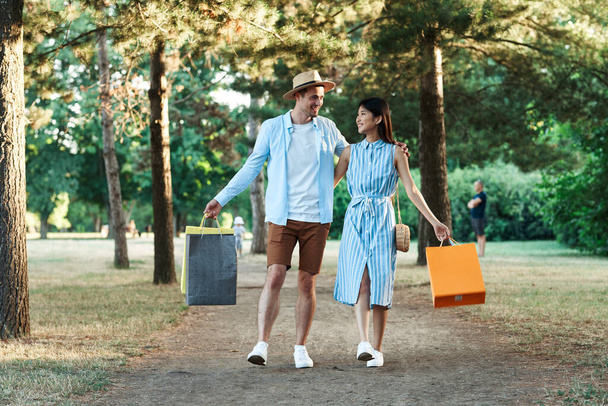 νεαρό ζευγάρι με τσάντες ψώνια περπατώντας στο πάρκο.  - Φωτογραφία, εικόνα