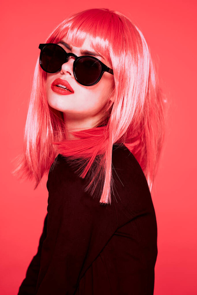 Νεαρή όμορφη γυναίκα με ροζ περούκα και γυαλιά ηλίου σε ροζ φόντο - Φωτογραφία, εικόνα