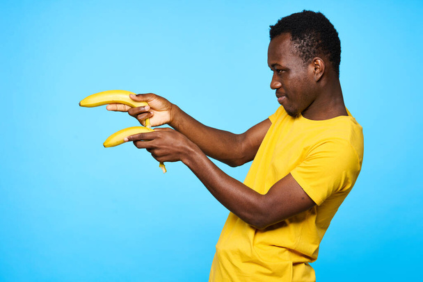 Nuori afrikkalainen mies osoittaa banaanit eristetty sinisellä pohjalla - Valokuva, kuva
