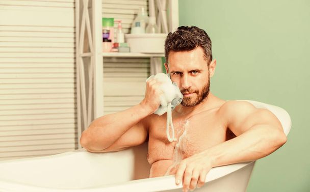 hygiene and health. Sexuality and relaxation concept. personal care. Sexy man in bathroom. desire and temptation. Macho sit naked in bathtub washing with sponge. man wash muscular body with sponge - Photo, Image