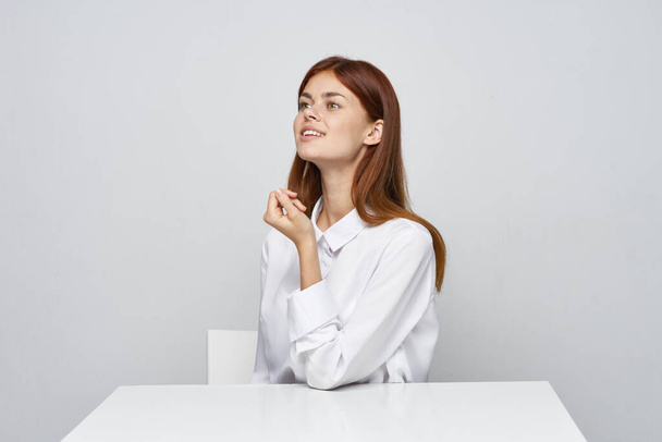 Молодая деловая женщина сидит за столом в офисе и смотрит в сторону             - Фото, изображение