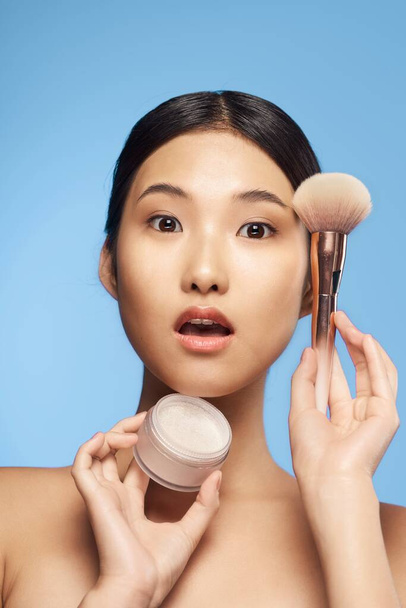 Young beautiful surprised asian woman  holding powder and brush    isolated  - 写真・画像