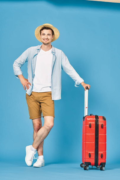 Студійний знімок молодого туриста з його червоною валізою
 - Фото, зображення