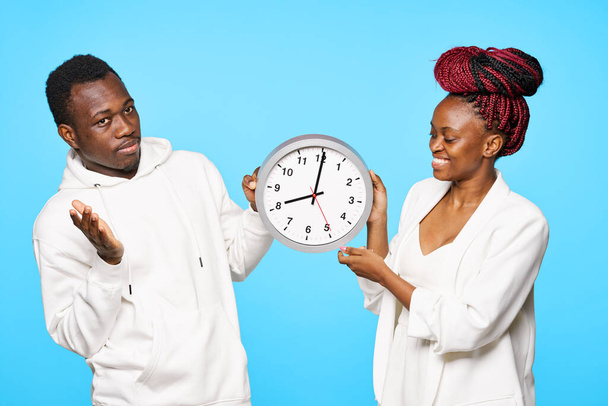 junges schönes Paar posiert mit Uhr im Studio auf blauem Hintergrund - Foto, Bild