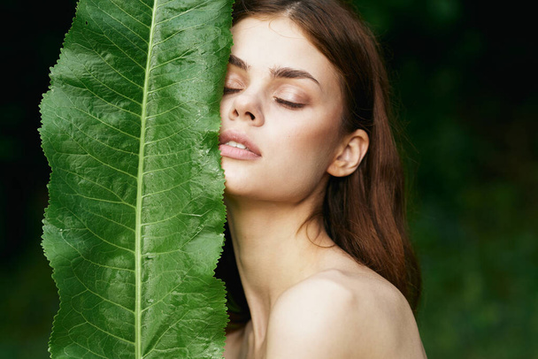 Молодая красивая женщина с закрытыми глазами держит зеленый лист в саду - Фото, изображение