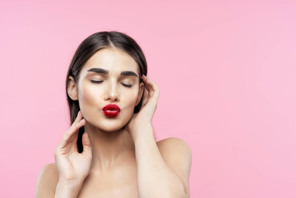Portrait of young beautiful woman showing kiss on pink  background  - 写真・画像