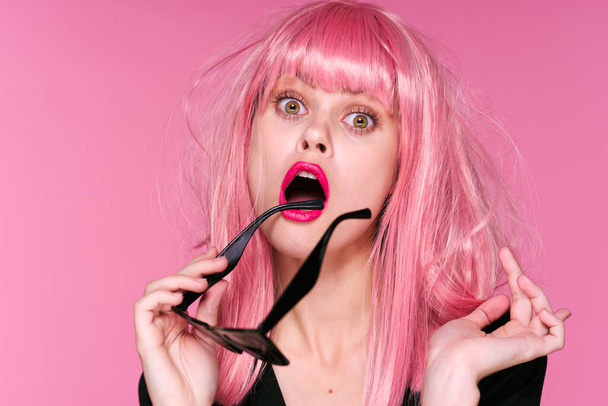 Sudio shot of beautiful woman in pink wig holding sunglasses  on pink background - Photo, Image