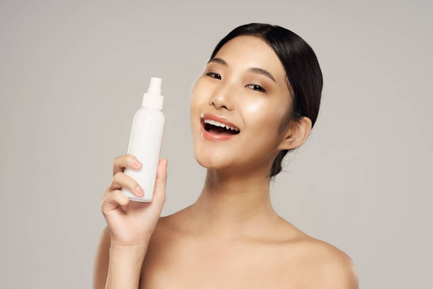 Young beautiful asian woman holding beauty product in studio on isolated background - Foto, Imagem