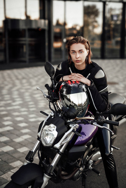 Chica segura en una chaqueta de moto se sienta con un casco de motocicleta en una moto - Foto, imagen