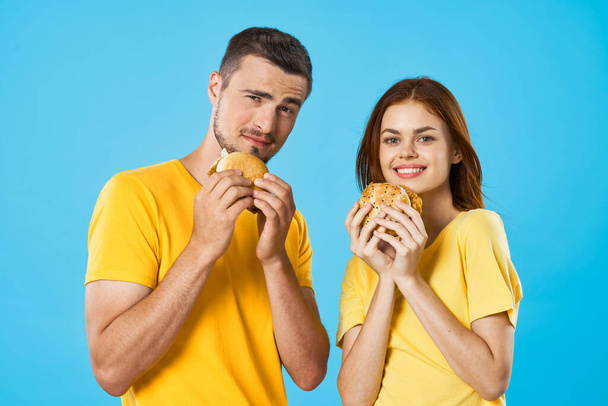 Young beautiful couple eating hamburgers. Studio shot - Foto, imagen