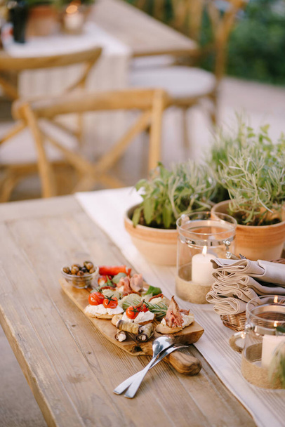 Tabla de cortar de madera con embutidos y cubiertos en la mesa por las flores en las macetas. - Foto, Imagen