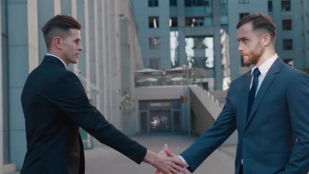 Two business partner shake hands when meeting. Portrait of handshake of two successful businessmen making a deal. Office building on the background. Business district. - Footage, Video