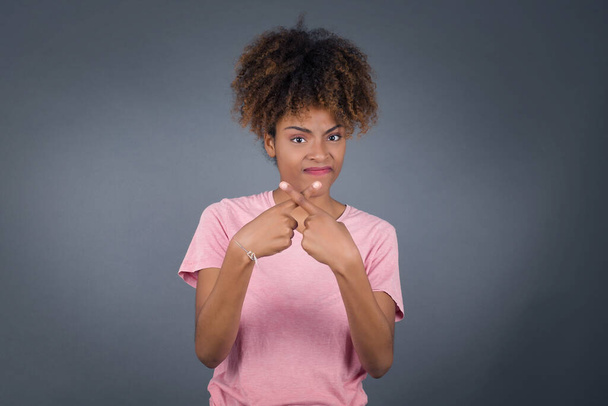 Jeune belle femme afro-américaine sur fond isolé debout contre un mur gris. A rejet expression en colère croisement des doigts faisant signe négatif. - Photo, image