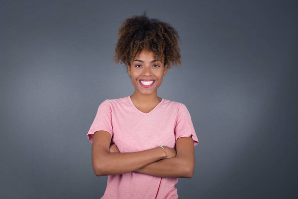 Профиль улыбающейся африканской американки со здоровой чистой кожей и скрещенными руками, стоящей над серой стеной студии - Фото, изображение