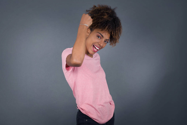 Сверхрадостная счастливая молодая красивая афроамериканка рада получать хорошие новости, активно жестикулирует от счастья, сжимает кулак и делает победный жест. Концепция реакции. - Фото, изображение