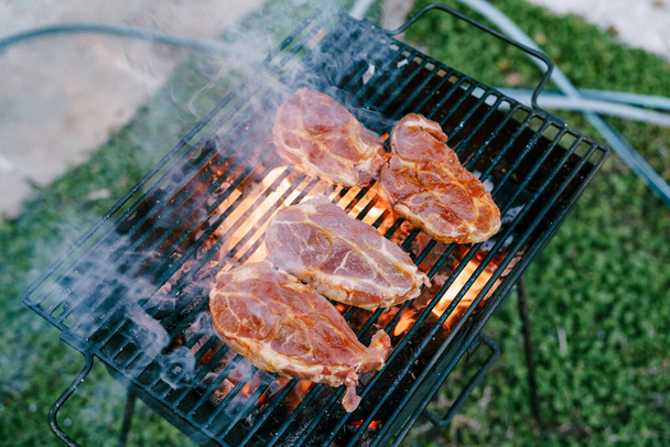 Rauwe steaks worden gegrild op een open vuur met rook. - Foto, afbeelding
