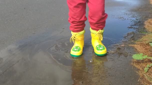 das Kind lacht und stapft in gelben Stiefeln durch Pfützen - Filmmaterial, Video