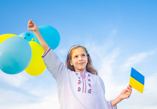 Дівчина в українській вишитій сорочці тримає жовто-синій прапор і кулі. - Фото, зображення