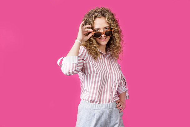 Portrait of a young, beautiful, healthy woman holding glasses and looking at the camera. Isolated on pink background. - Photo, Image