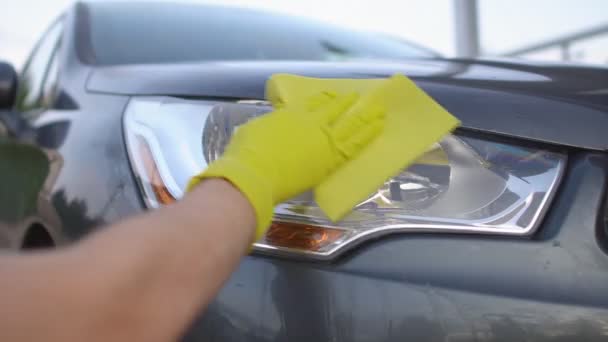 Lähikuva miehen käsi keltainen käsine pesu auton ajovalo. Auton puhdistus käsite - Materiaali, video