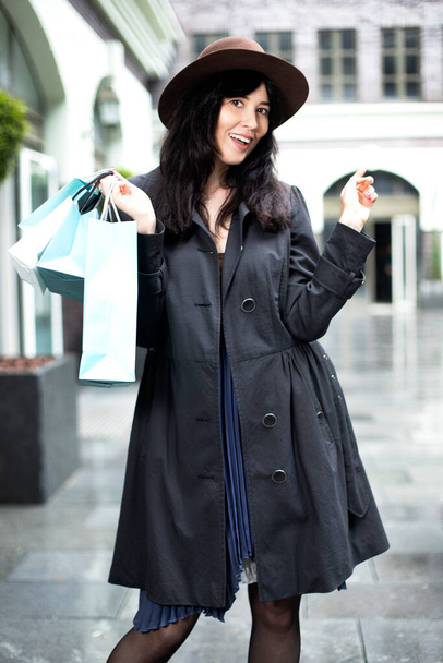 красива дівчина в пальто і капелюсі насолоджується покупками
 - Фото, зображення