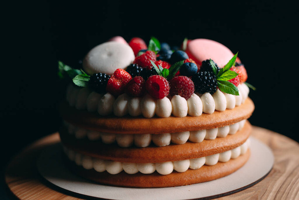 Fruit cake. Cake decorated with berries on a wooden stand on a black background. - Zdjęcie, obraz