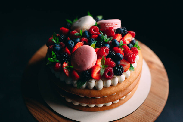 Fruit cake. Cake decorated with berries on a wooden stand on a black background. - Fotografie, Obrázek