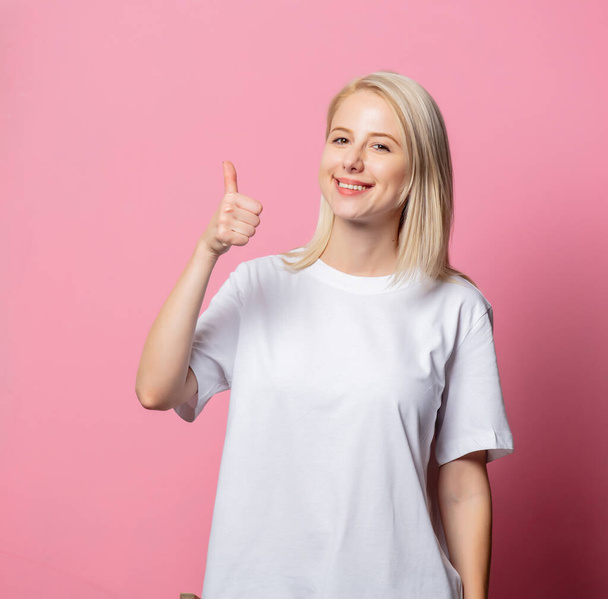 ブロンド女性でホワイトmoch-up tシャツ上のピンクの背景  - 写真・画像