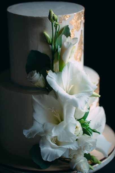 two-tier cake with flowers on a wooden stand on a black background. - Φωτογραφία, εικόνα
