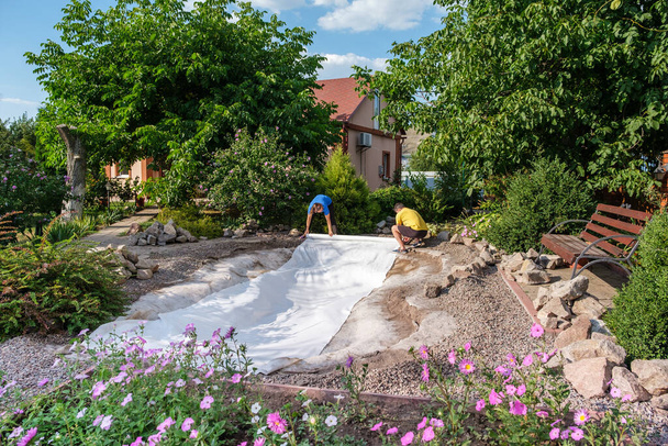 Family roll out a roll of white non-woven geotextile fabric to set up fish pond - Photo, Image