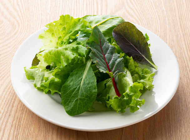 Διάφορα φύλλα σαλάτας σε ένα πιάτο που σε ένα ξύλινο φόντο - Φωτογραφία, εικόνα