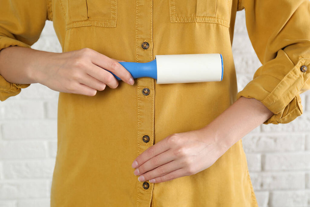 Woman cleaning yellow shirt with lint roller against white brick wall, closeup - Foto, Bild