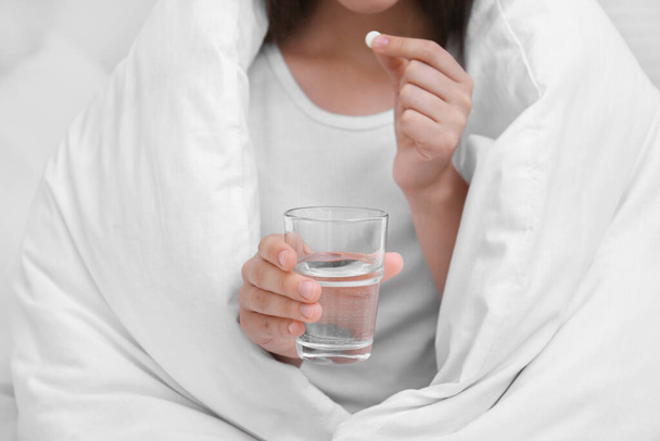 Woman with glass of water taking pill in bedroom, closeup - Foto, immagini