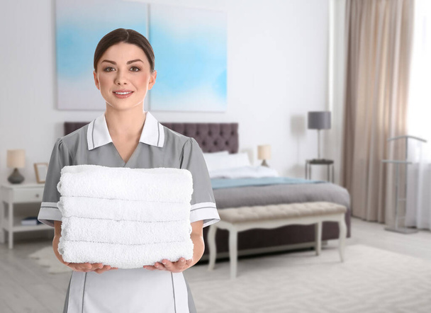 Beautiful chambermaid with clean folded towels near bed in hotel room - Foto, Bild
