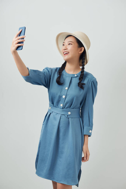 Happy beautiful girl in casual or hipster style, pigtail hairstyle, standing, holding mobile smart phone and doing selfie - Фото, зображення