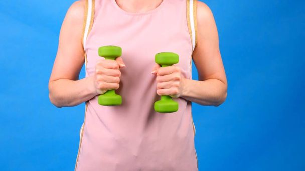 Nainen vaaleanpunainen urheilupuku käsipainoilla käsissä tekee harjoituksia sinisellä taustalla. Käsite urheilu, ruokavalio ja laihtuminen - Valokuva, kuva