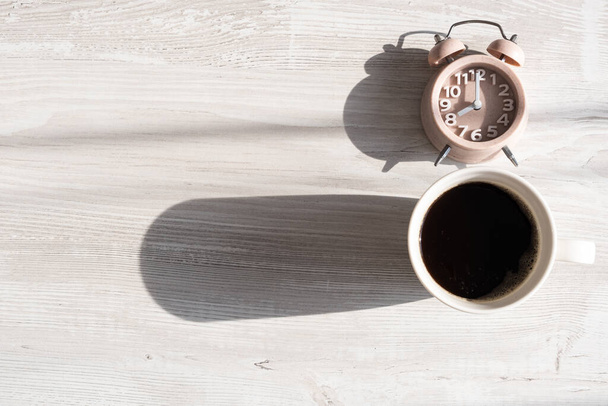 Close-up van een wekker en een kopje koffie heeft late avond en zonsondergang zonlicht. Werk laat in de avond, recycling, kopieerruimte - Foto, afbeelding