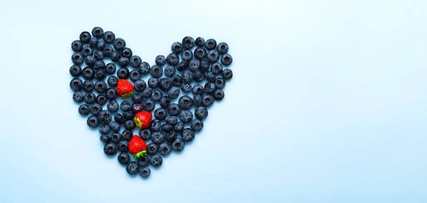 Konceptualne jedzenie. Świeże jagody w kształcie serca na niebieskim tle. Zbliżenie - Zdjęcie, obraz