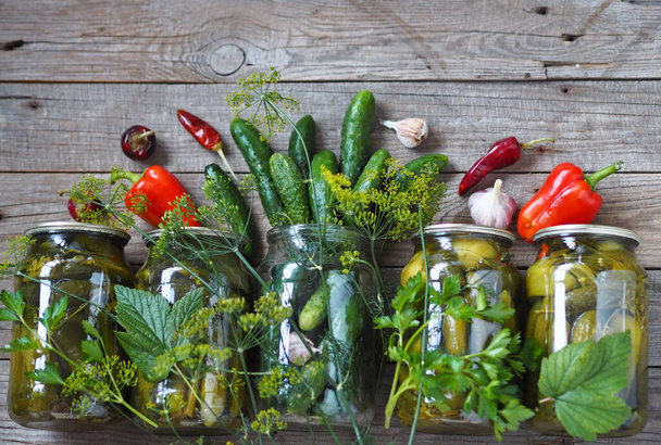 Home remedies for future use. Fresh and pickled cucumbers, homemade canned food with cucumbers in glass jars on a wooden background. - Fotoğraf, Görsel