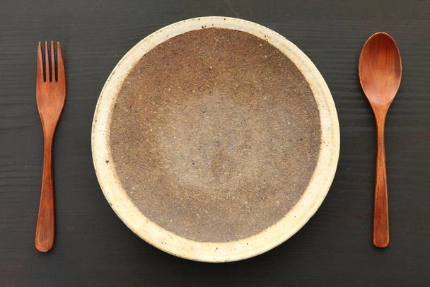 empty clay dish with wooden cutlery on a dining table - Φωτογραφία, εικόνα