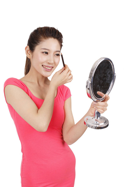 Fiatal nő rózsaszín ruhában kezében egy tükör, alkalmazó smink - Fotó, kép