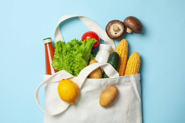 Хлопковый мешок с различными продуктами питания на синем фоне, вид сверху - Фото, изображение