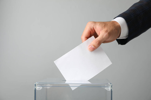Mann legt Stimmzettel in Wahlurne auf grauem Hintergrund - Foto, Bild