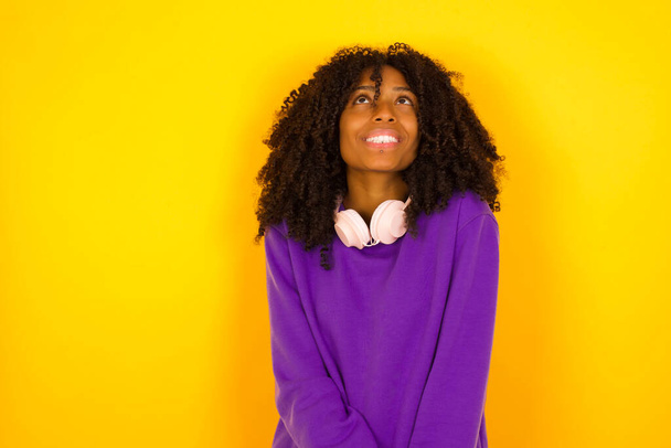 Femme afro-américaine a le sourire rêveur sur fond jaune. Concept d'émotions et de gestes - Photo, image