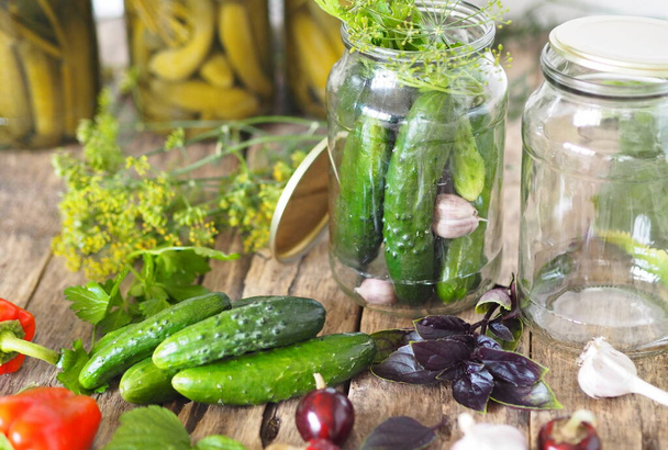 Home remedies for future use. Fresh and pickled cucumbers, homemade canned food with cucumbers in glass jars on a wooden background. - Foto, imagen